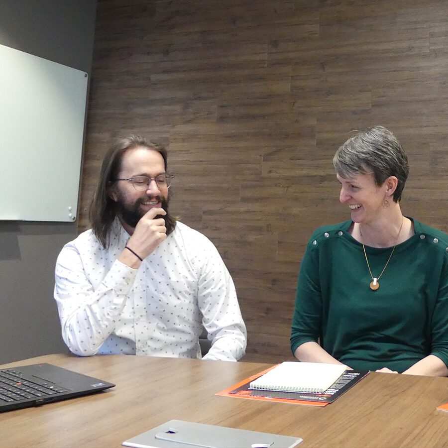 Man and woman sitting in a conference room, smiling.