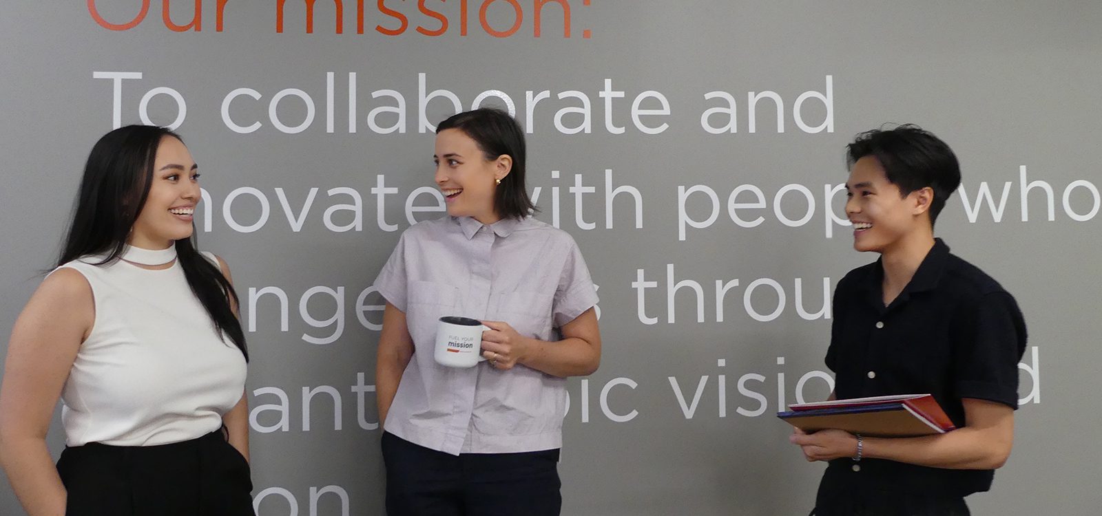 Three people standing in front of a mission statement and smiling
