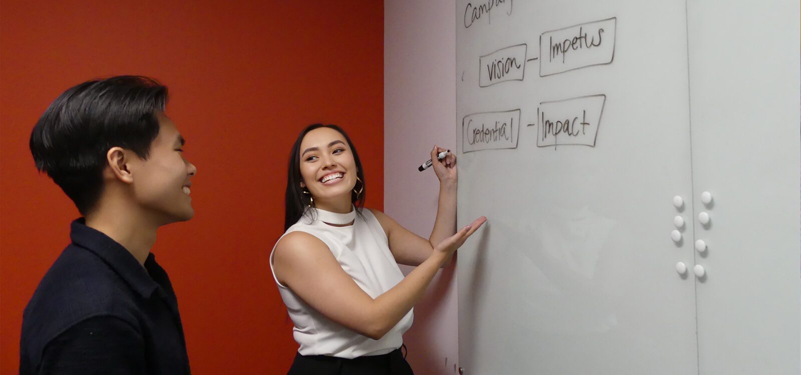 Two people smiling and collaborating in front of a whiteboard