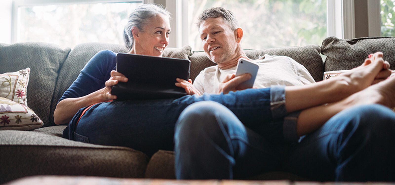 Man and woman are sitting down holding a tablet and phone.